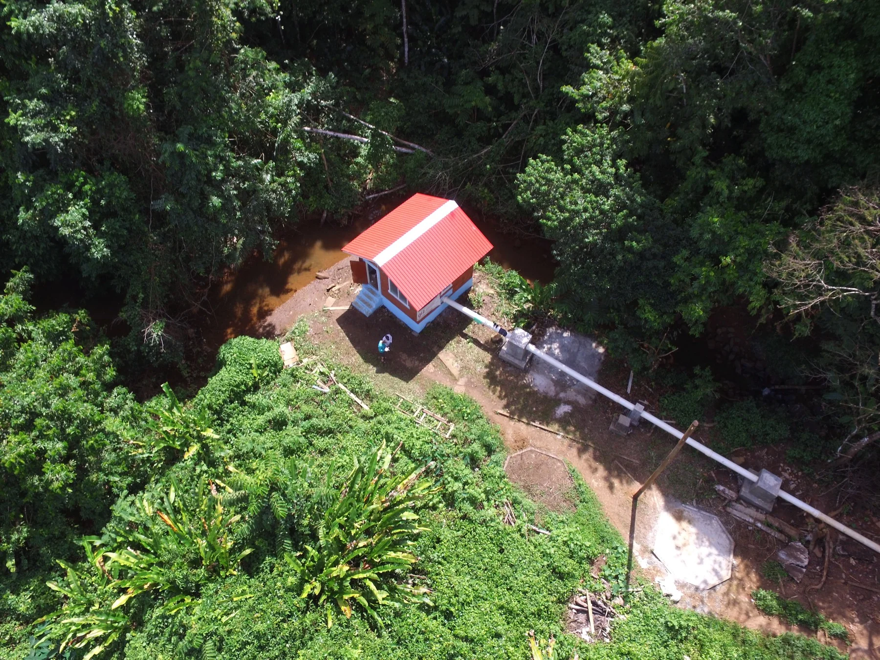 Aerial view of Hosororo's red-roofed powerhouse and penstock surrounded by rainforest in Guyana